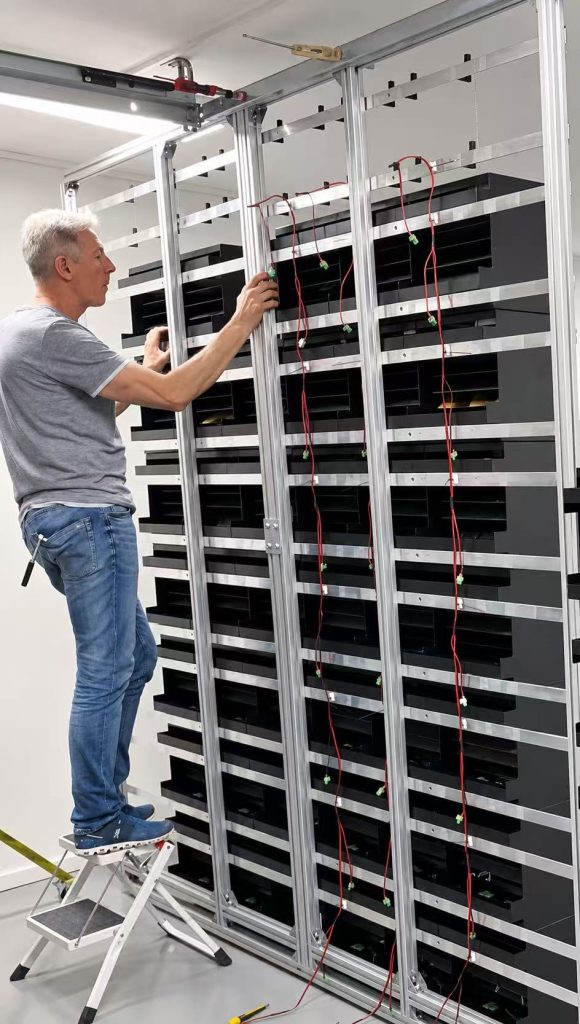 Technician installing Picture Flap modules and wiring onto the rear aluminum frame for a Porsche Design display