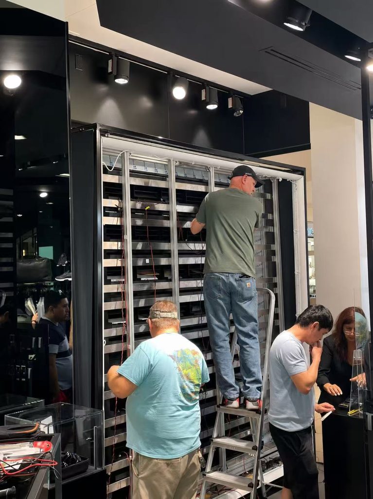 Installation team assembling and connecting the rear structure of a Porsche Design Picture Flap Display inside a retail store