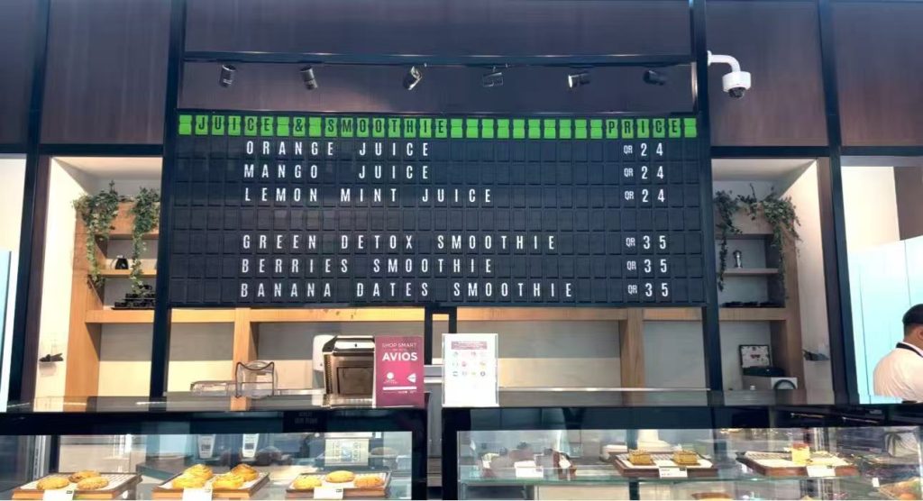 Custom split flap menu board displaying juice and smoothie prices inside a restaurant, designed as a mechanical airport-style menu display.