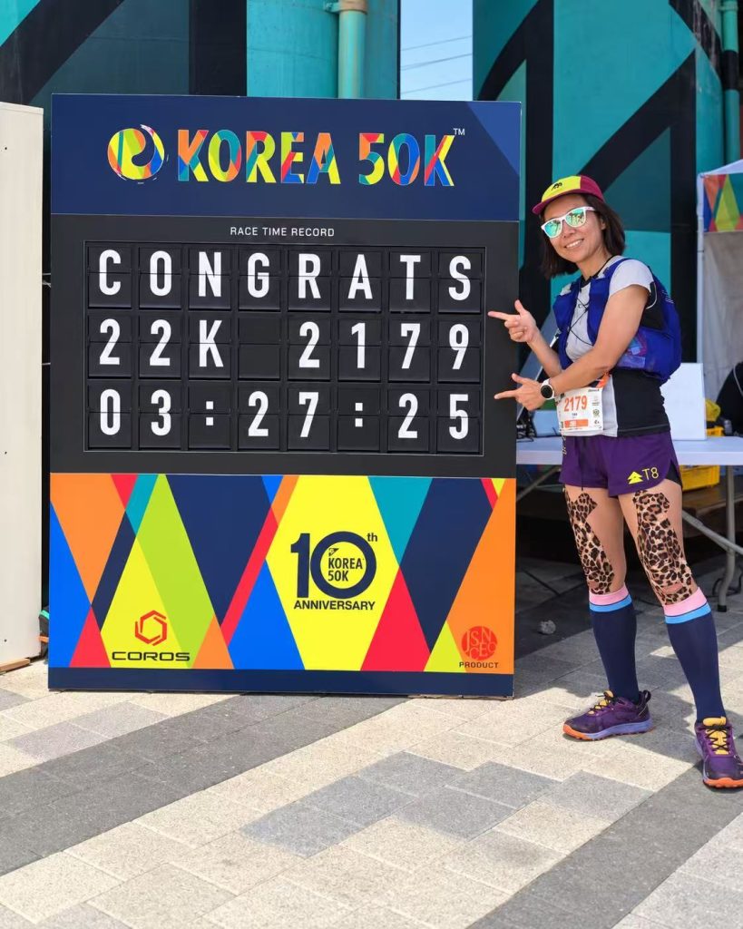 Female runner posing beside a TS Display split flap board showing her 22K race result and finishing time.